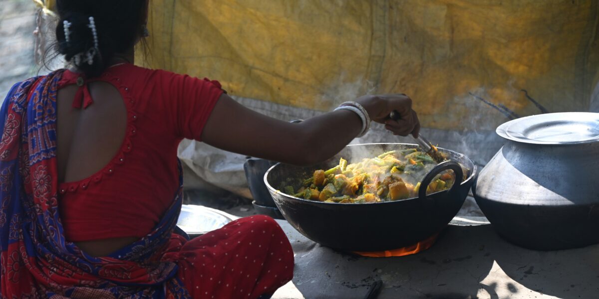 Indian woman cooking over a wood-burning fire surrounded by smoke, illustrating household air pollution from biomass cooking fuels in rural India