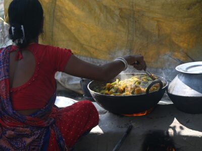 Indian woman cooking over a wood-burning fire surrounded by smoke, illustrating household air pollution from biomass cooking fuels in rural India