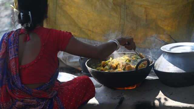 Indian woman cooking over a wood-burning fire surrounded by smoke, illustrating household air pollution from biomass cooking fuels in rural India