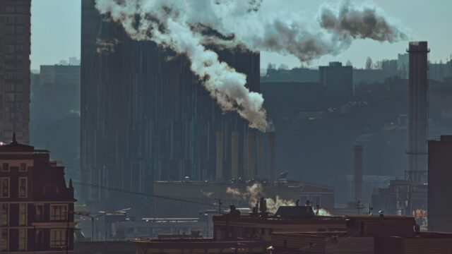 Industrial cityscape with multiple smokestacks releasing smoke into a hazy sky representing how GDP growth capitalism harms public health across food work environment housing and healthcare